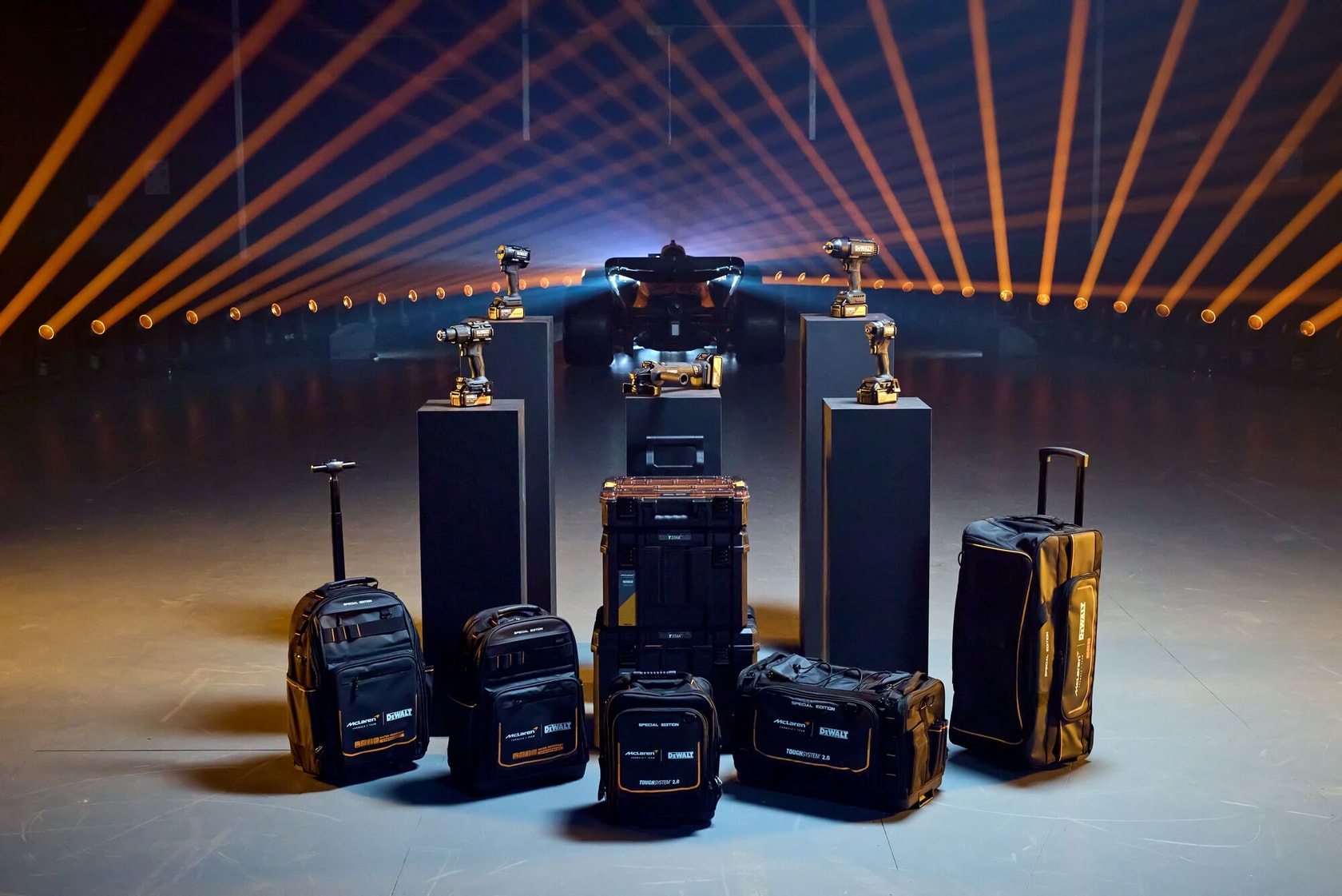 Bolsas y cajas DEWALT con taladros ante un auto de carreras y luces llamativas.